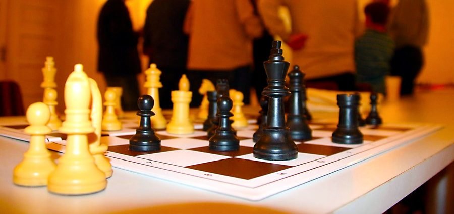 Aufgebaute Schachpartie, dahinter die Spielerinnen und Spieler.